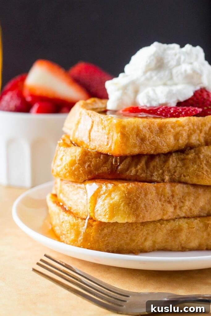 Classic French Toast Recipe: Crispy Edges and Creamy Center 3 A tall stack for french toast topped with whipped cream and strawberries, then drizzled in maple syrup.
