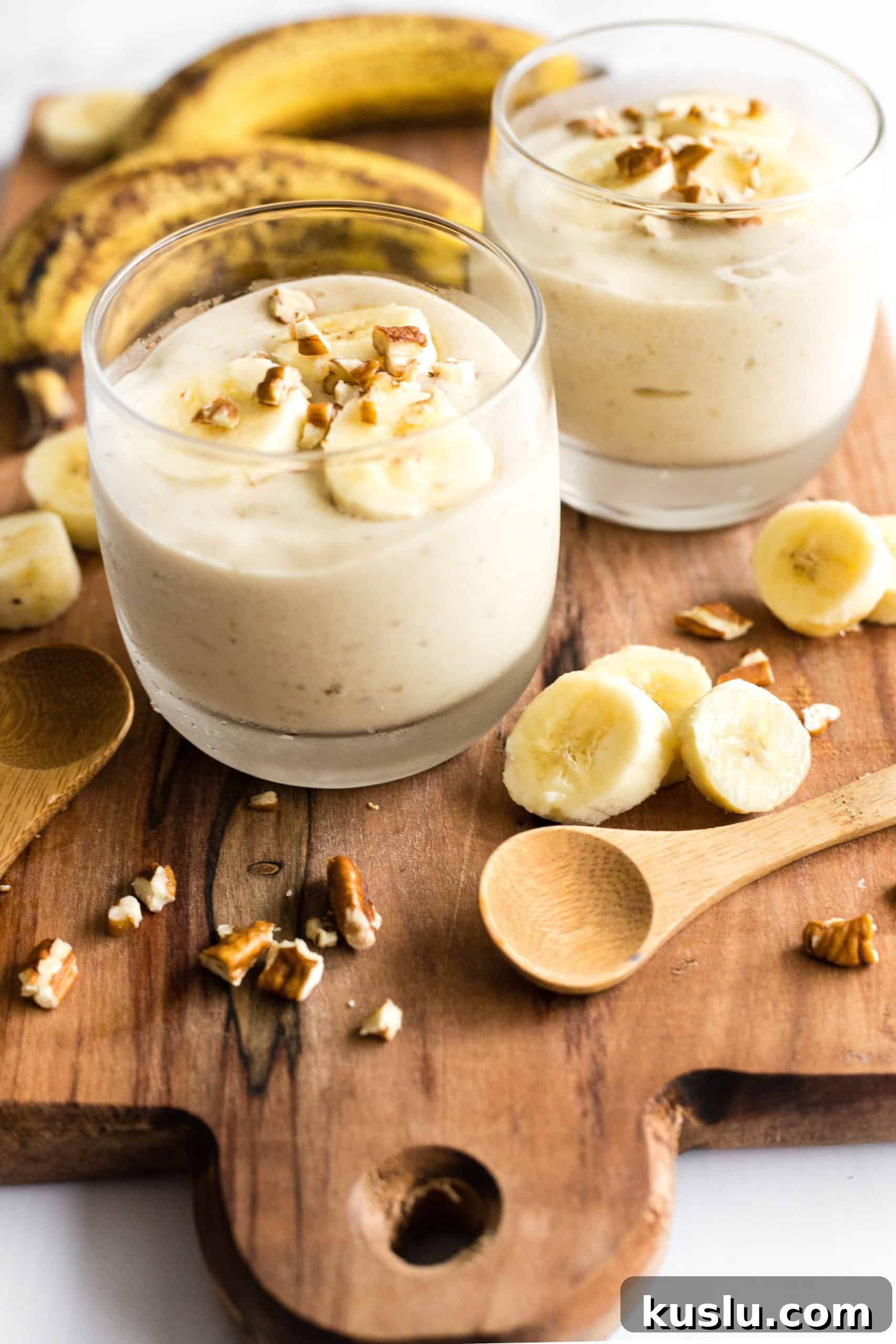 Two glasses with vegan banana ice cream on wooden board.
