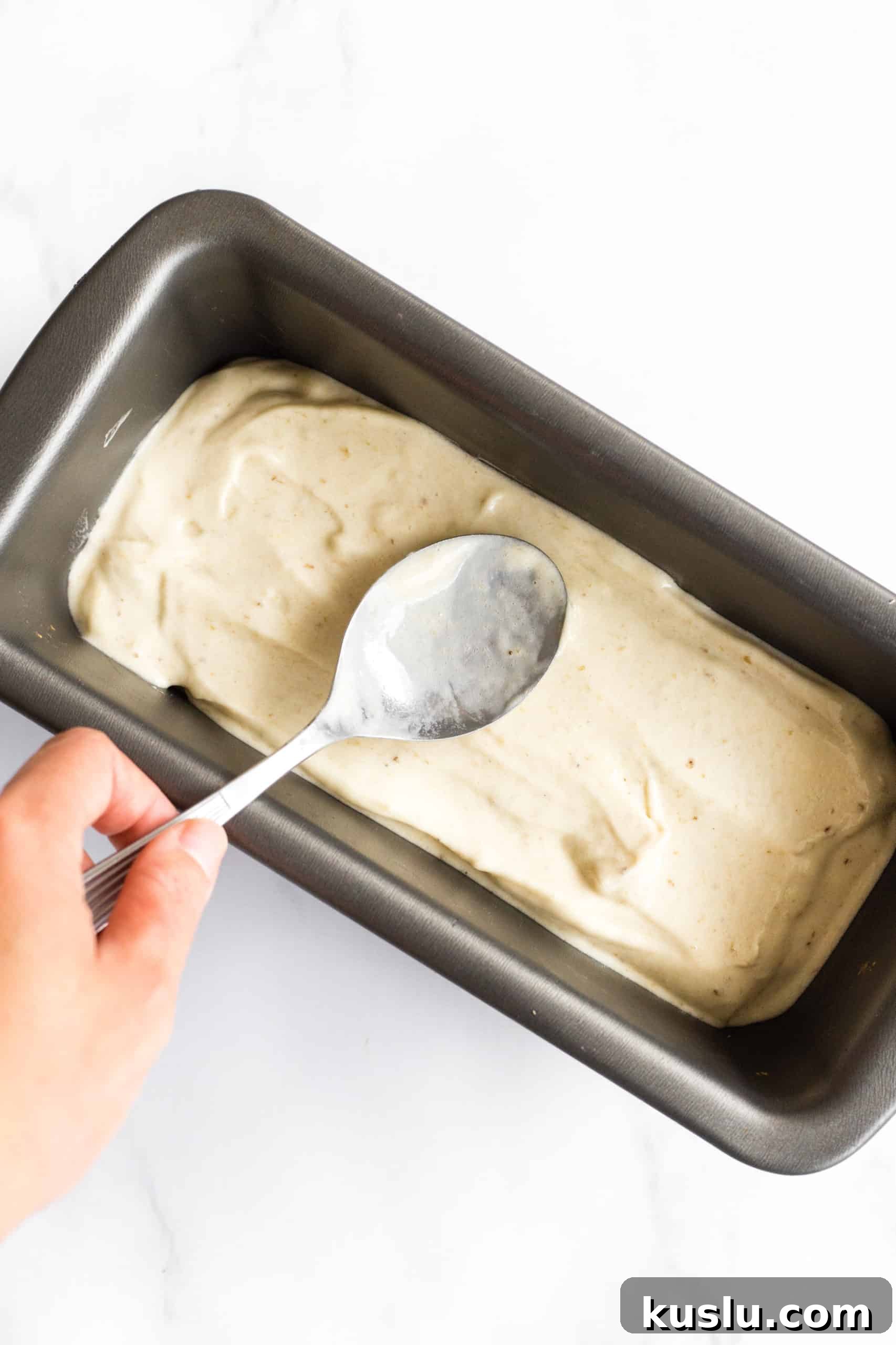 Using a spoon to spread out no-churn banana ice cream in a loaf pan to be frozen.