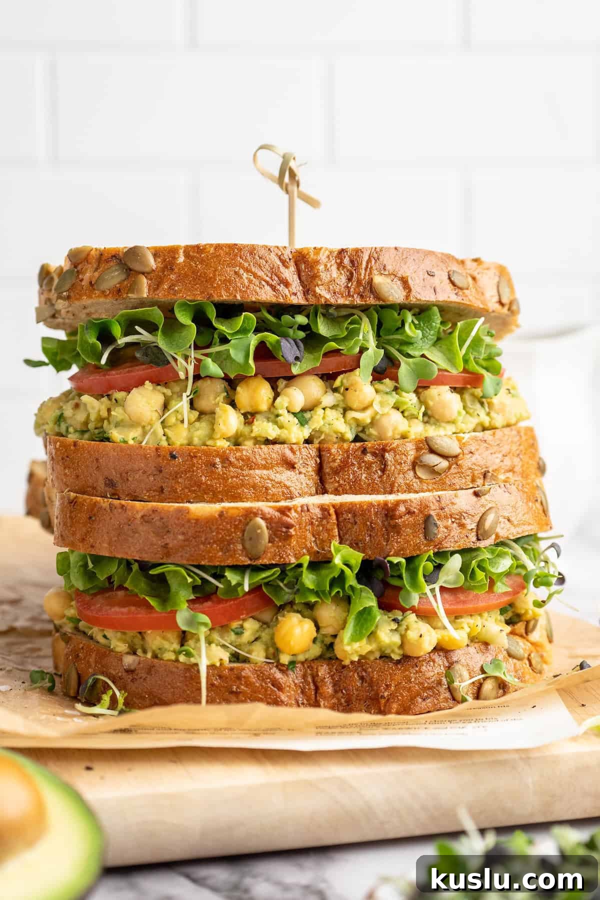 Two smashed chickpea avocado salad sandwiches stacked on cutting board