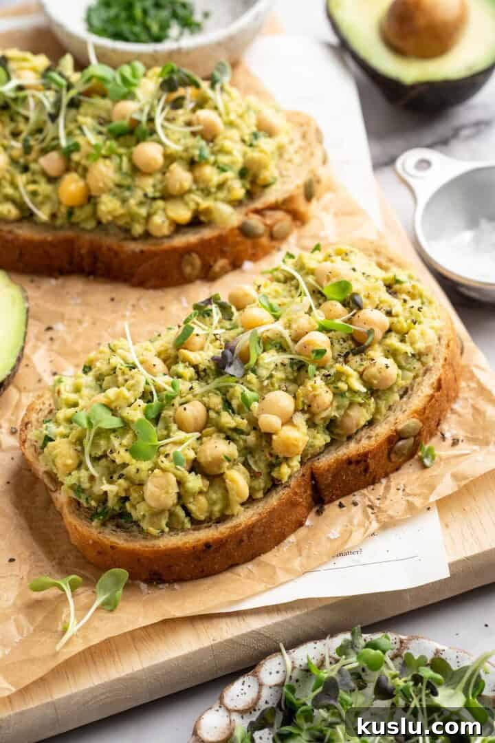 Two slices of bread topped with smashed chickpea avocado salad and microgreens