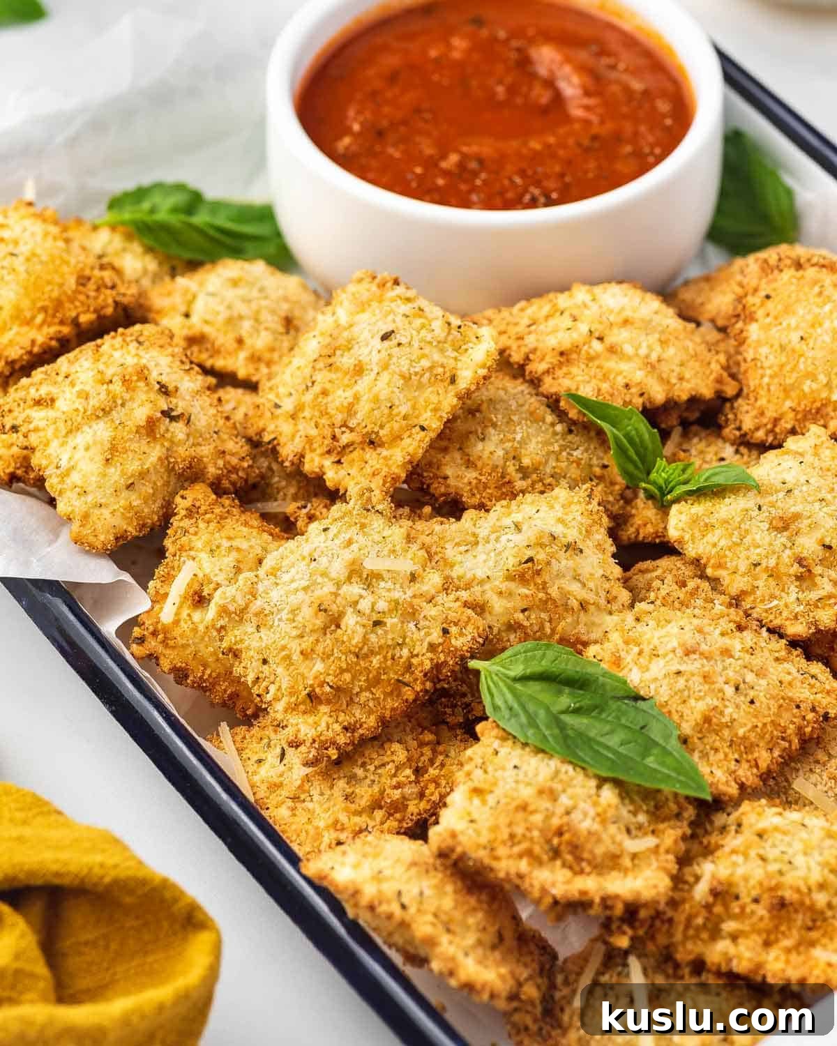A tray of air fryer ravioli with a small bowl of marinara.