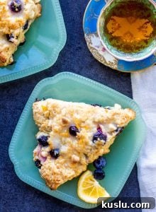 Overhead shot of two blueberry scones on teal plates with a cup of tea.
