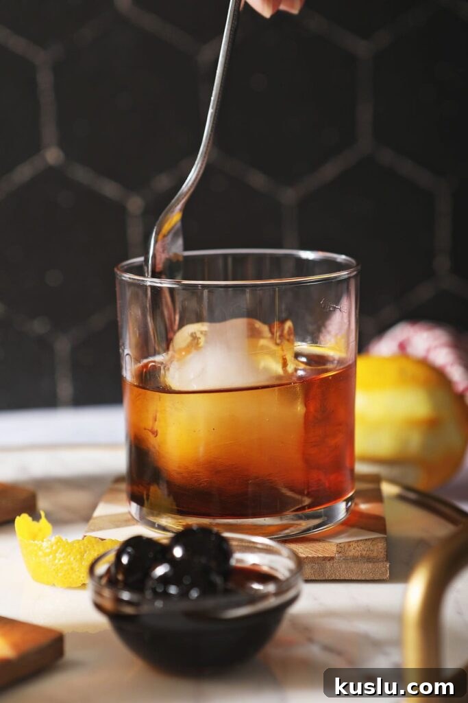 Busted Pipe Bourbon & Amaro Cocktail Recipe 5 A spoon stirs an amaro cocktail with a huge ice cube