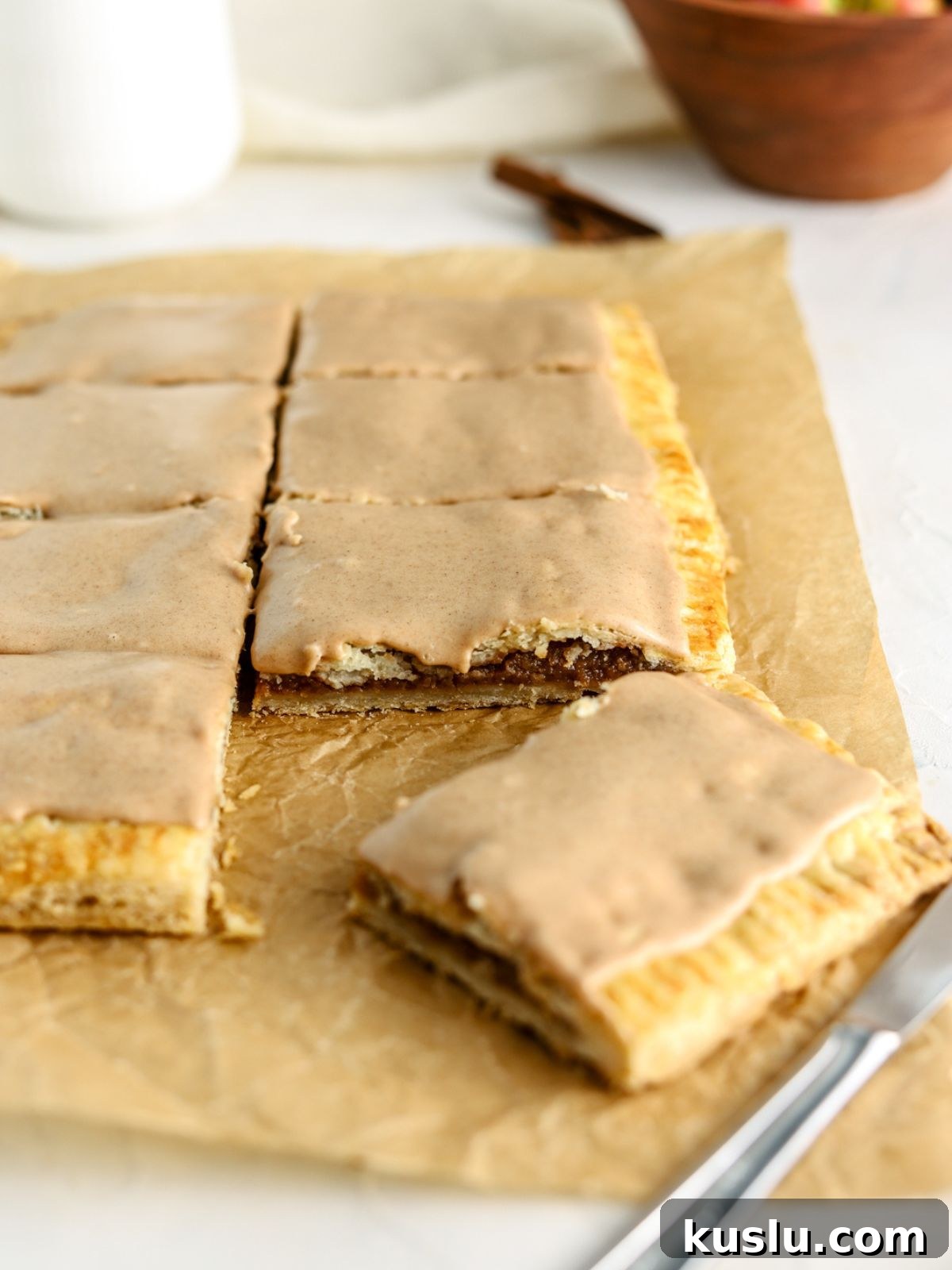 Homemade Apple Pop-Tarts Recipe for Flaky Pastry Filling 6 A giant pop tart with cinnamon icing cut into slices on parchment paper.