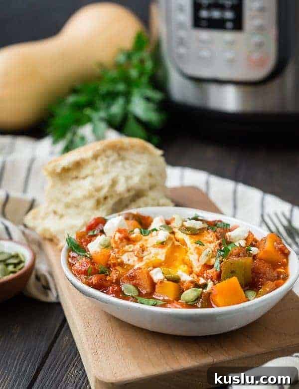 Small white oval bowl with fall-inspired shakshuka with squash, tomato sauce, and eggs. Bread is also pictured.