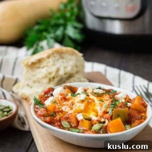Small white oval bowl filled with tomato sauce, cubed squash, an egg, feta cheese, and pepitas.