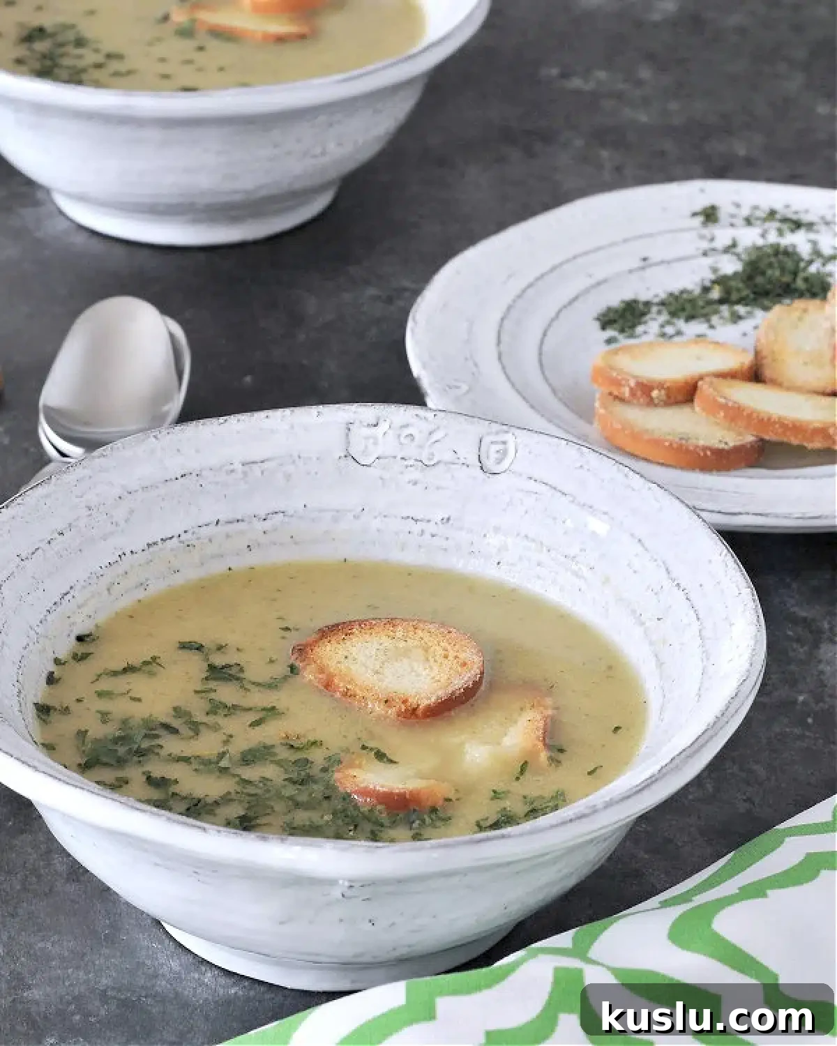 Artichoke soup in bowls garnished with crisp bagel chips and chopped herbs.