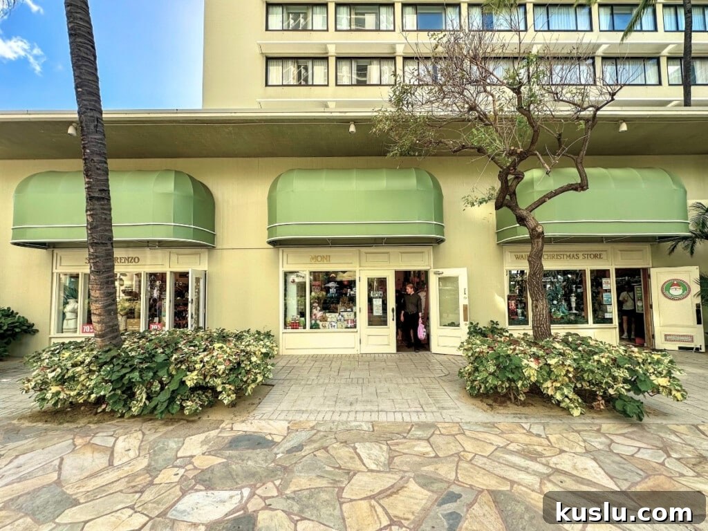 Moana Surfrider shopping area in Waikīkī featuring boutique stores including San Lorenzo Bikinis & Waikiki Christmas Store with green awnings and elegant store fronts.