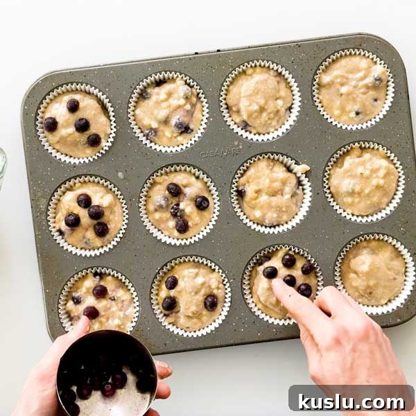 Adding additional blueberries to the top of the blueberry muffin batter in the pan.