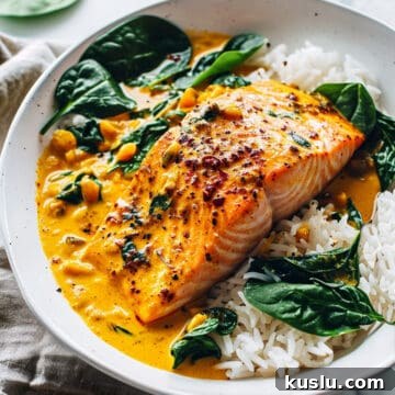 Coconut salmon curry in a creamy curry sauce on a white plate with spinach and rice.