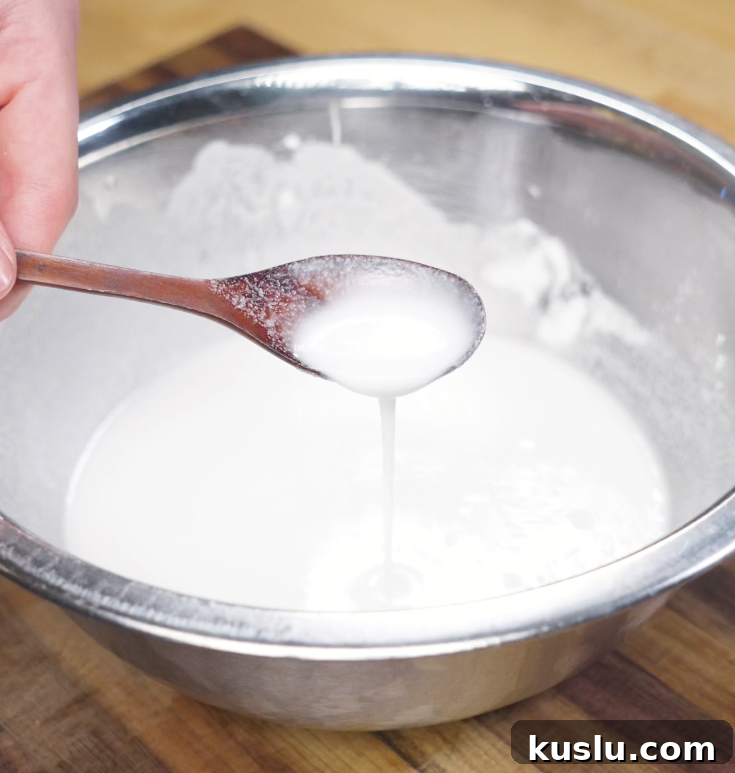 Crispy Korean Fried Chicken Recipe: How to Make Dakgangjeong 5 A spoon drips a slightly thin white batter made from rice flour, potato starch, salt, and water into a large bowl.