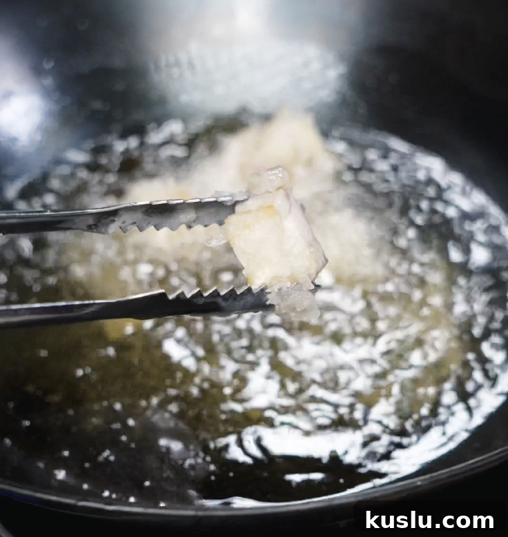 Crispy Korean Fried Chicken Recipe: How to Make Dakgangjeong 6 A single battered chicken piece is lifted from hot oil during the first fry at 350°F, still pale and crisping up.