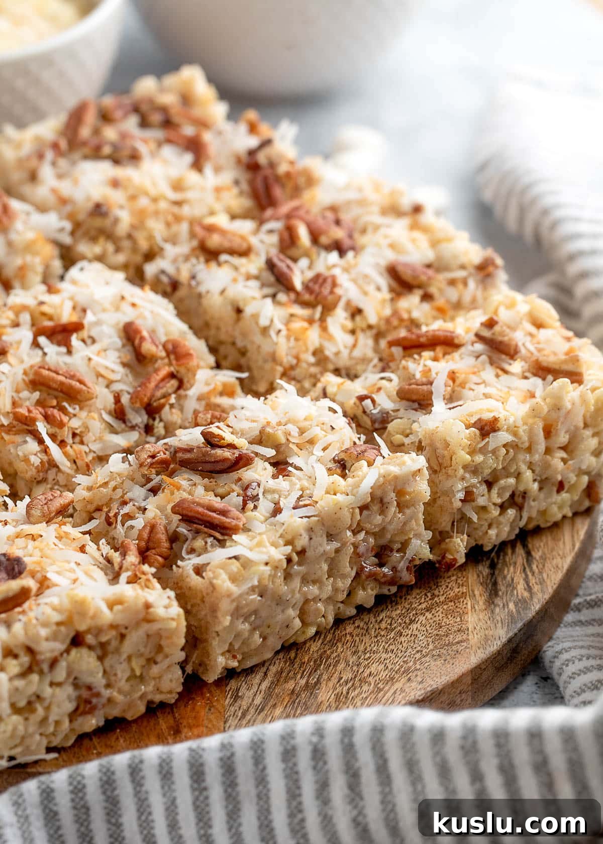 Coconut Pecan Rice Krispie Treats Recipe for Crispy Sweets 2 coconut pecan rice krispie treats cut into squares on a wood serving board with a gray and white striped napkin