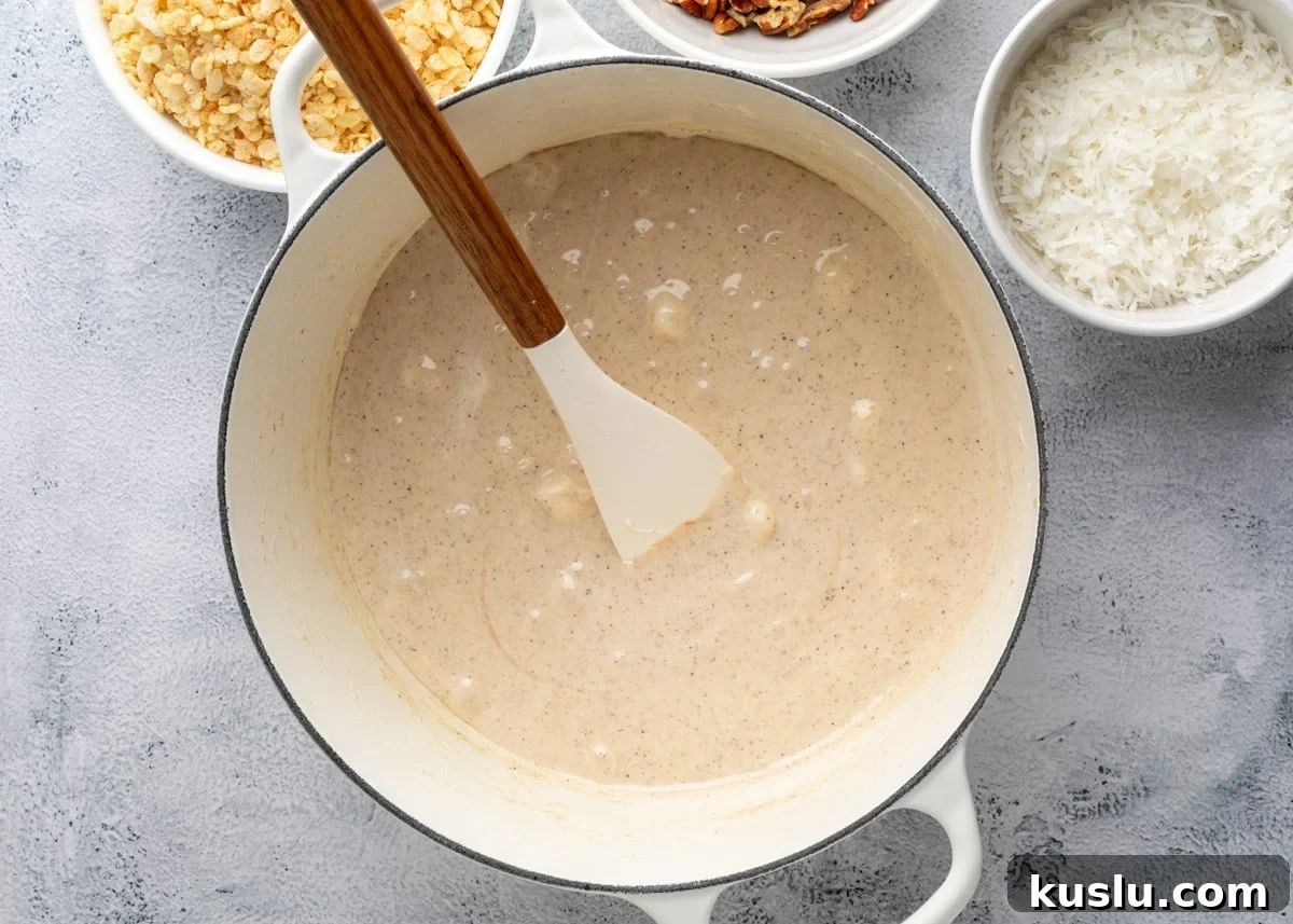 Coconut Pecan Rice Krispie Treats Recipe for Crispy Sweets 8 overhead of melted marshmallows in a white enameled cast iron pot with a wood handled spatula