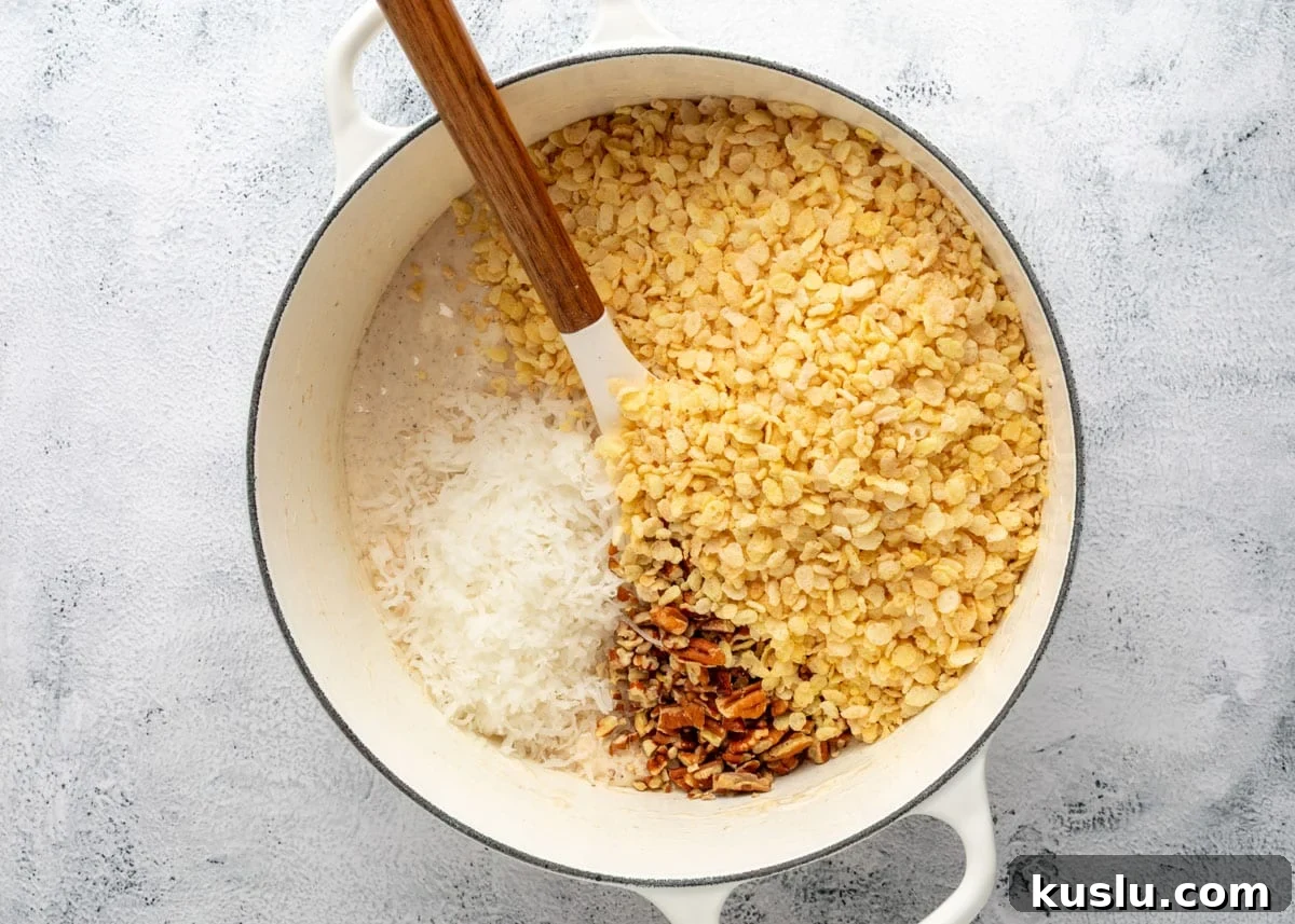 Coconut Pecan Rice Krispie Treats Recipe for Crispy Sweets 9 Rice Krispies cereal, shredded coconut, and toasted pecans added to melted marshmallows in a white enameled cast iron pot with a wood handled spatula