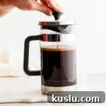 Someone pressing down on a french press coffee maker plunger as they make coffee in a french press.