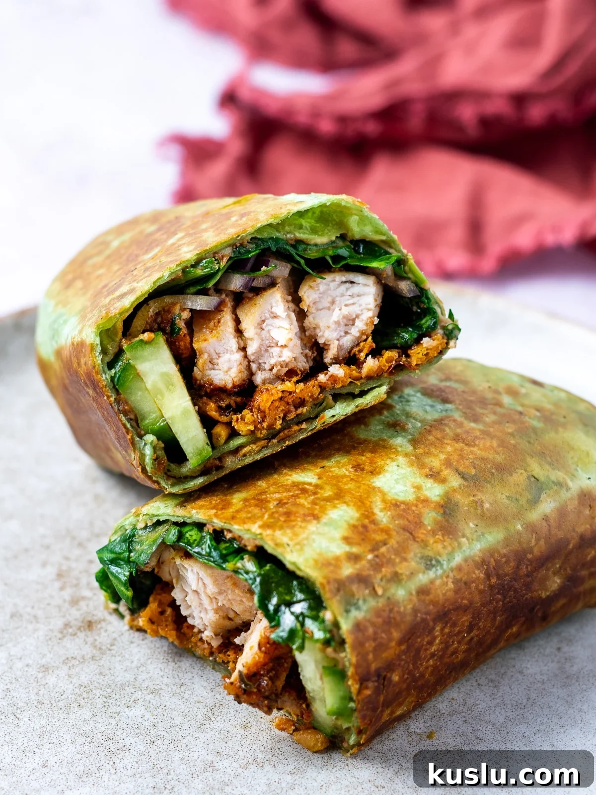 two halves of a toasted chicken wrap with crispy parmesan, spinach, hummus and cucumbers