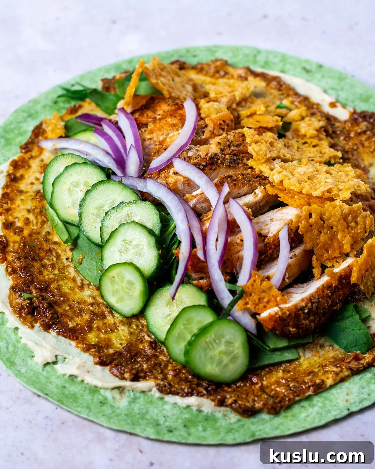 garden spinach herb tortilla spread with hummus, sun-dried tomato pesto, spinach, cucumbers, red onion, seasoned chicken and crispy parmesan