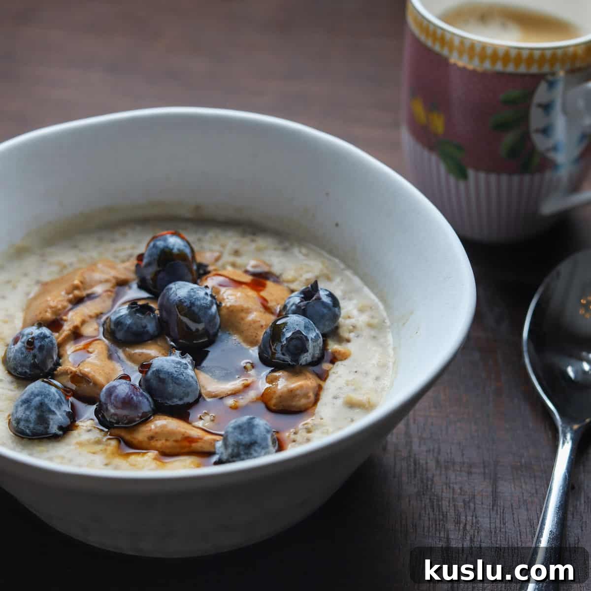Blueberry Oat & Chia Porridge with Almond Butter (Vegan) 4 Photo of a bowl of porridge with a coffee and spoon on a wooden table top.