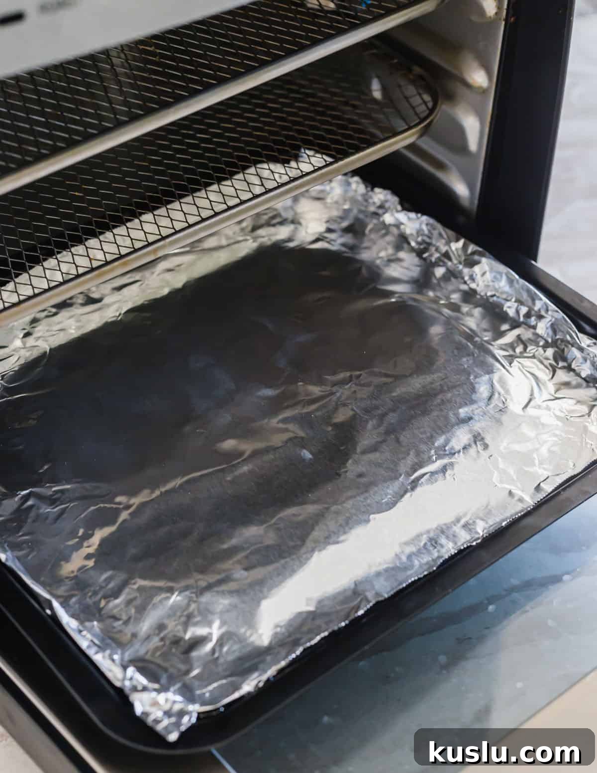Inside of an air fryer with aluminum foil lining the bottom tray for easy clean up. Inside of an air fryer with aluminum foil lining the bottom tray for easy clean up.