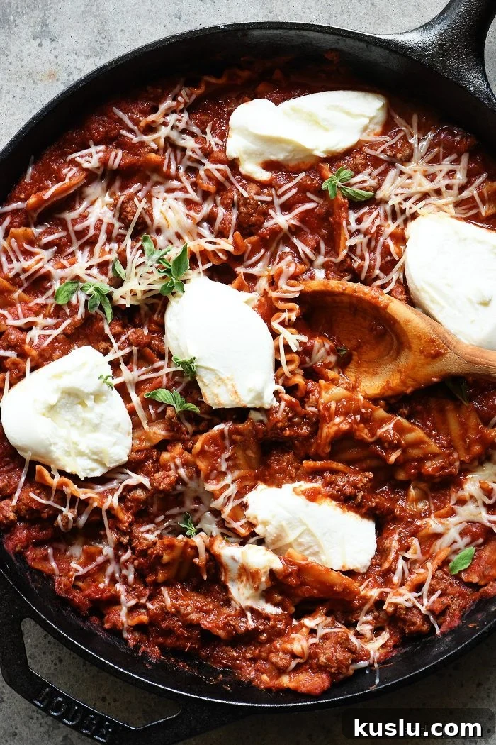 One-Pan Skillet Lasagna: Quick Comfort Dinner Recipe 3 Iron skillet holds lasagna, meat sauce, ricotta cheese and parmesan as well as a wooden spoon.