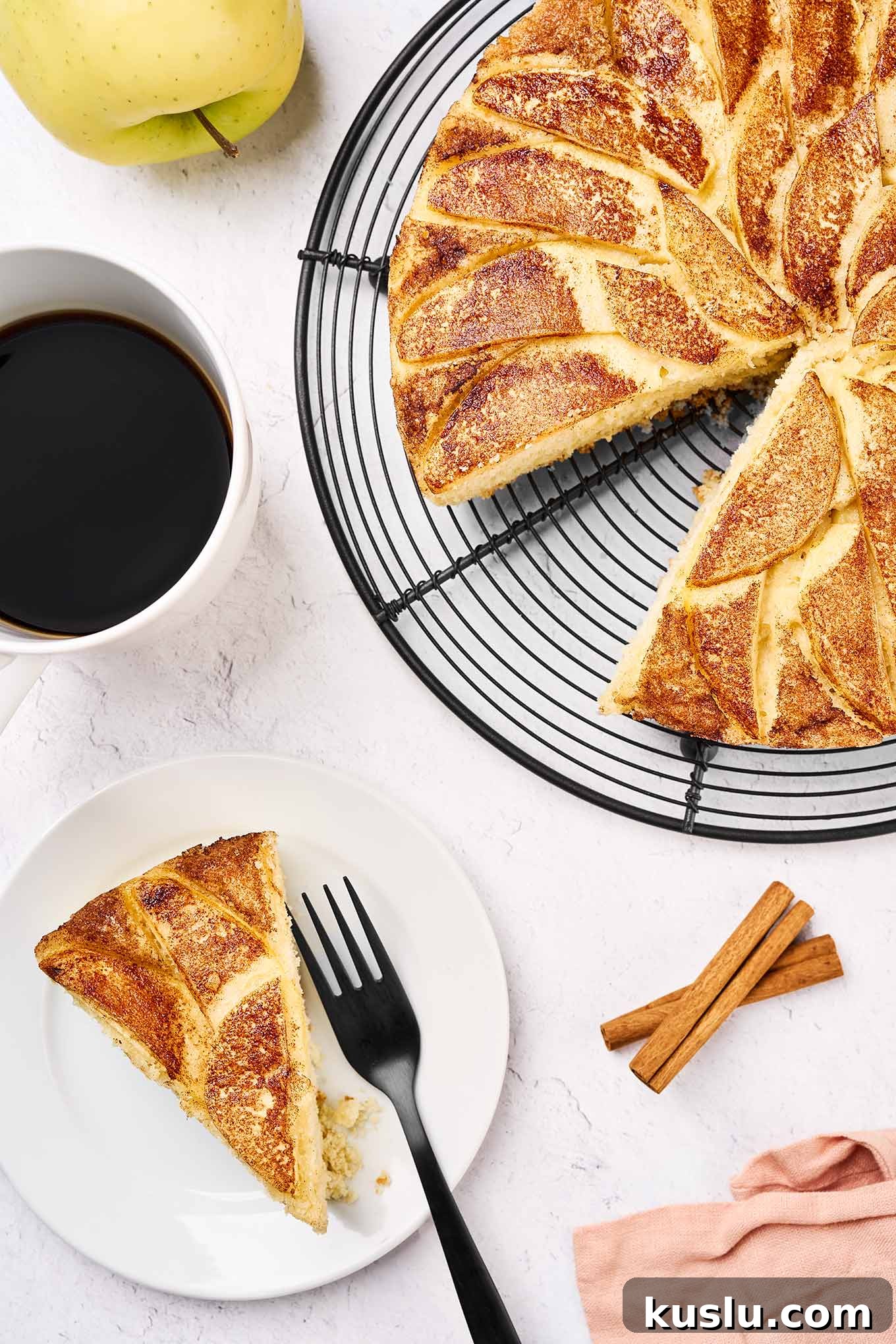 Moist Golden Delicious Apple Cake Recipe for Fall Baking 2 A slice of Golden Delicious apple cake served with a cup of black coffee more cake to the right, cinnamon sticks and a whole apple in the background.