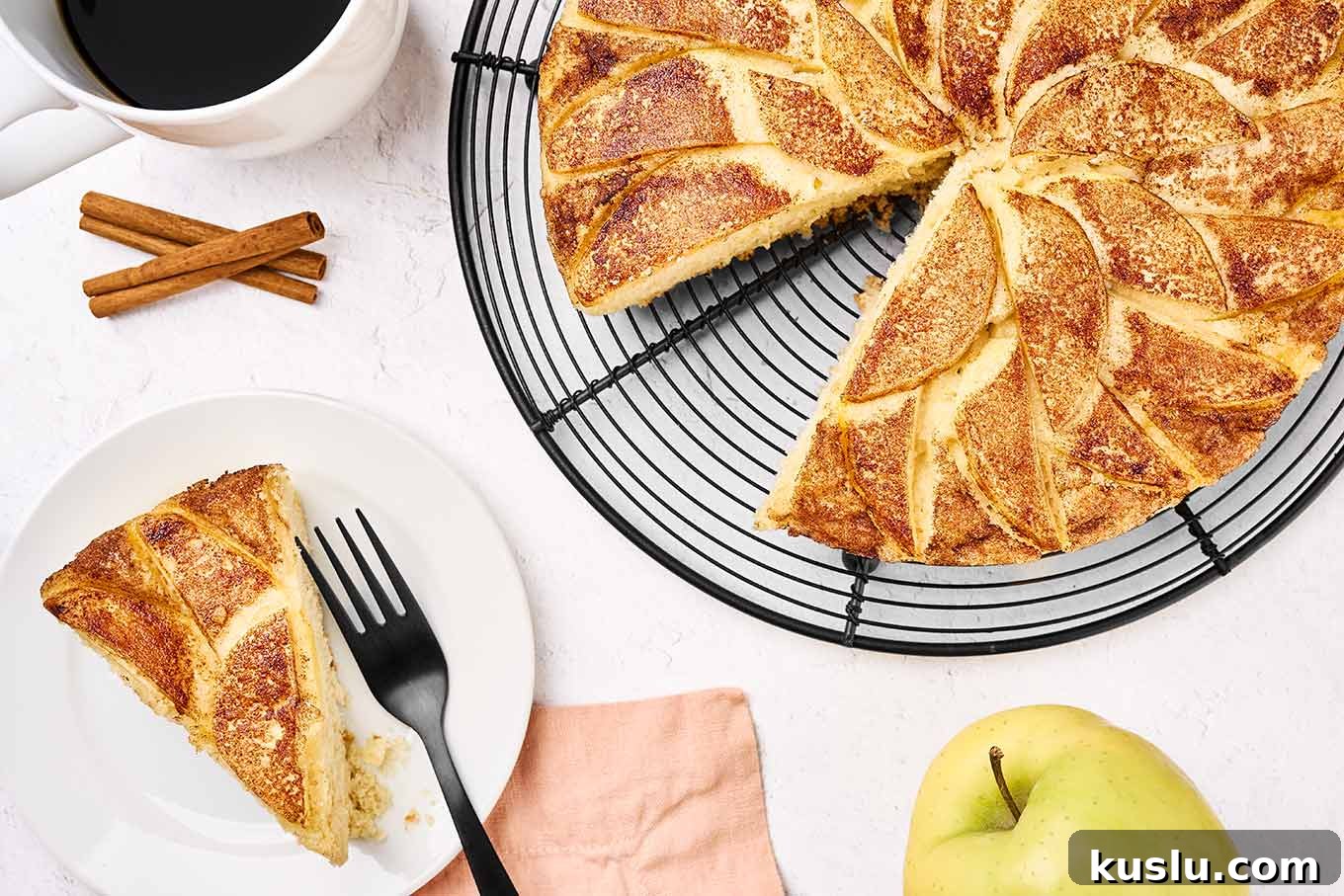 Moist Golden Delicious Apple Cake Recipe for Fall Baking 8 A slice of apple cake on a plate with a black fork, a cup of coffee in the corner, and the rest of the cake on a black wire cooling rack.