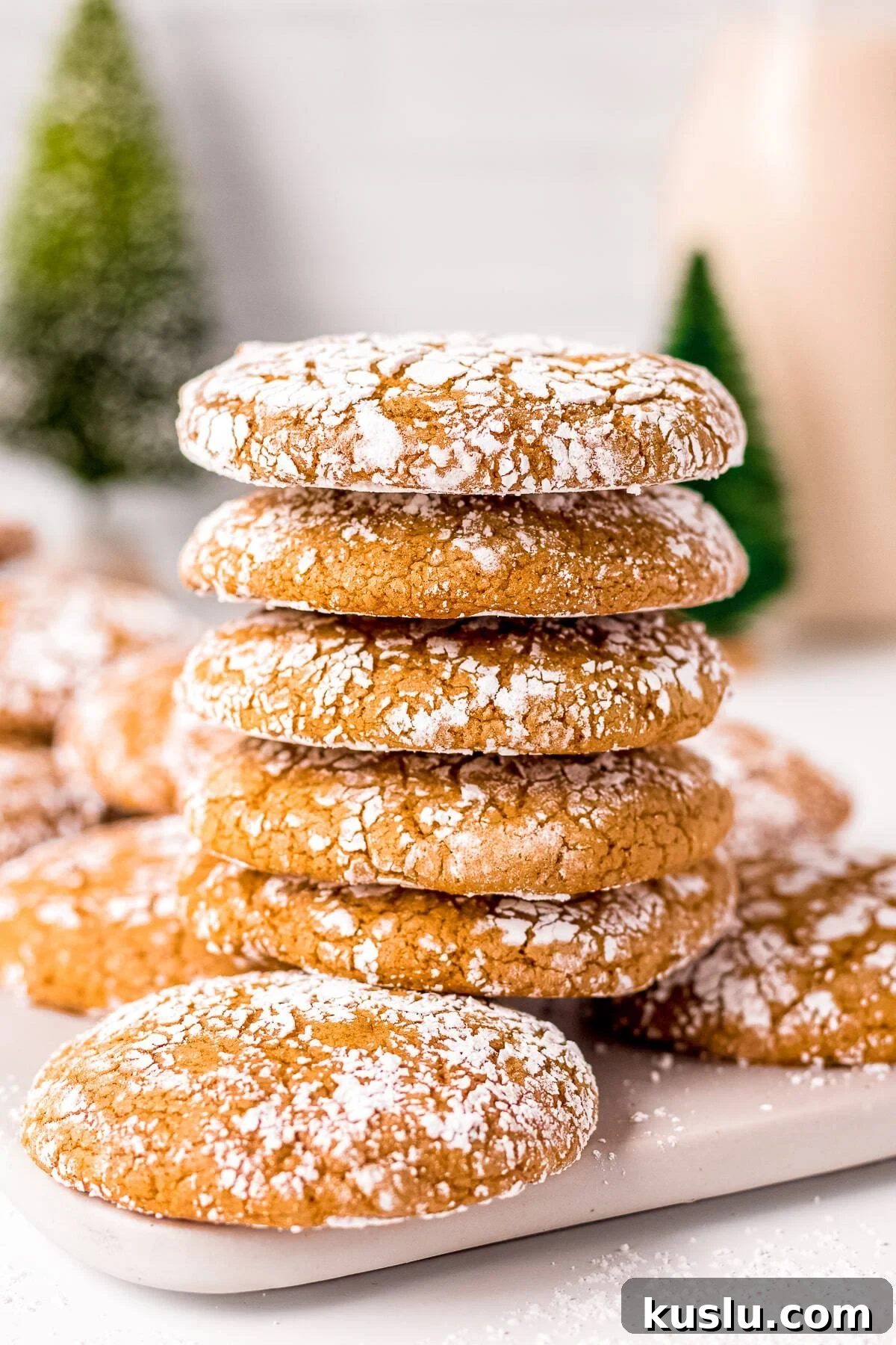 Five stacked Molasses Crinkle Cookies on top of other cookies on white board.