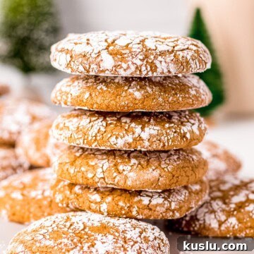 Five stacked Molasses Crinkle Cookies on top of other cookies on white board.