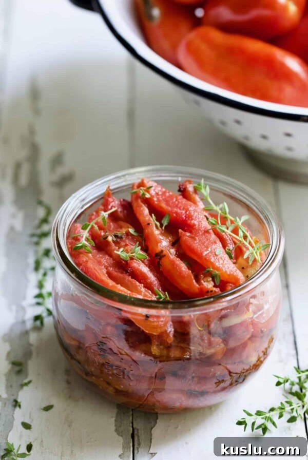 Tomato Confit in glass jar garnished with fresh thyme.