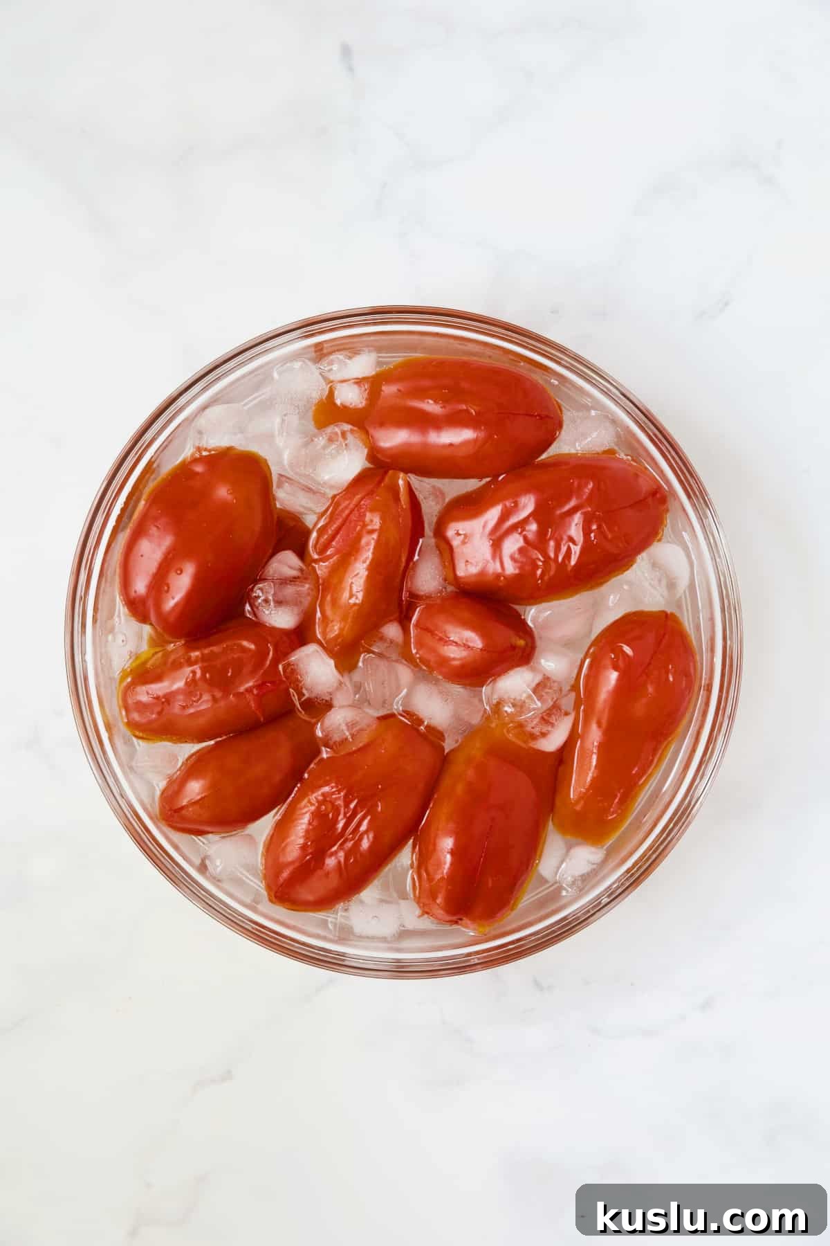 Roma tomatoes after being blanched in ice water in glass bowl.