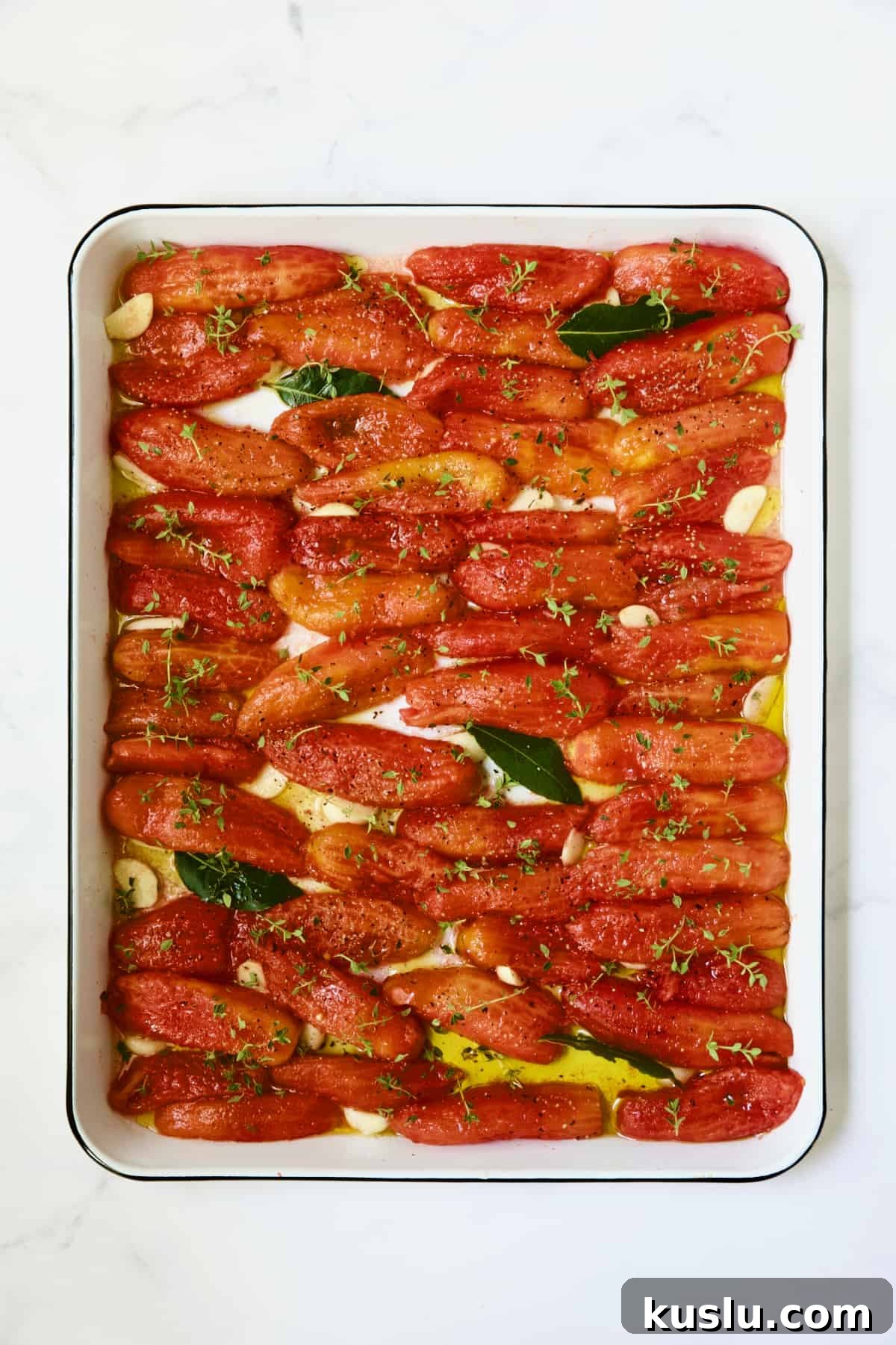 Tomatoes on white enameled baking sheet before being slow-roasted.