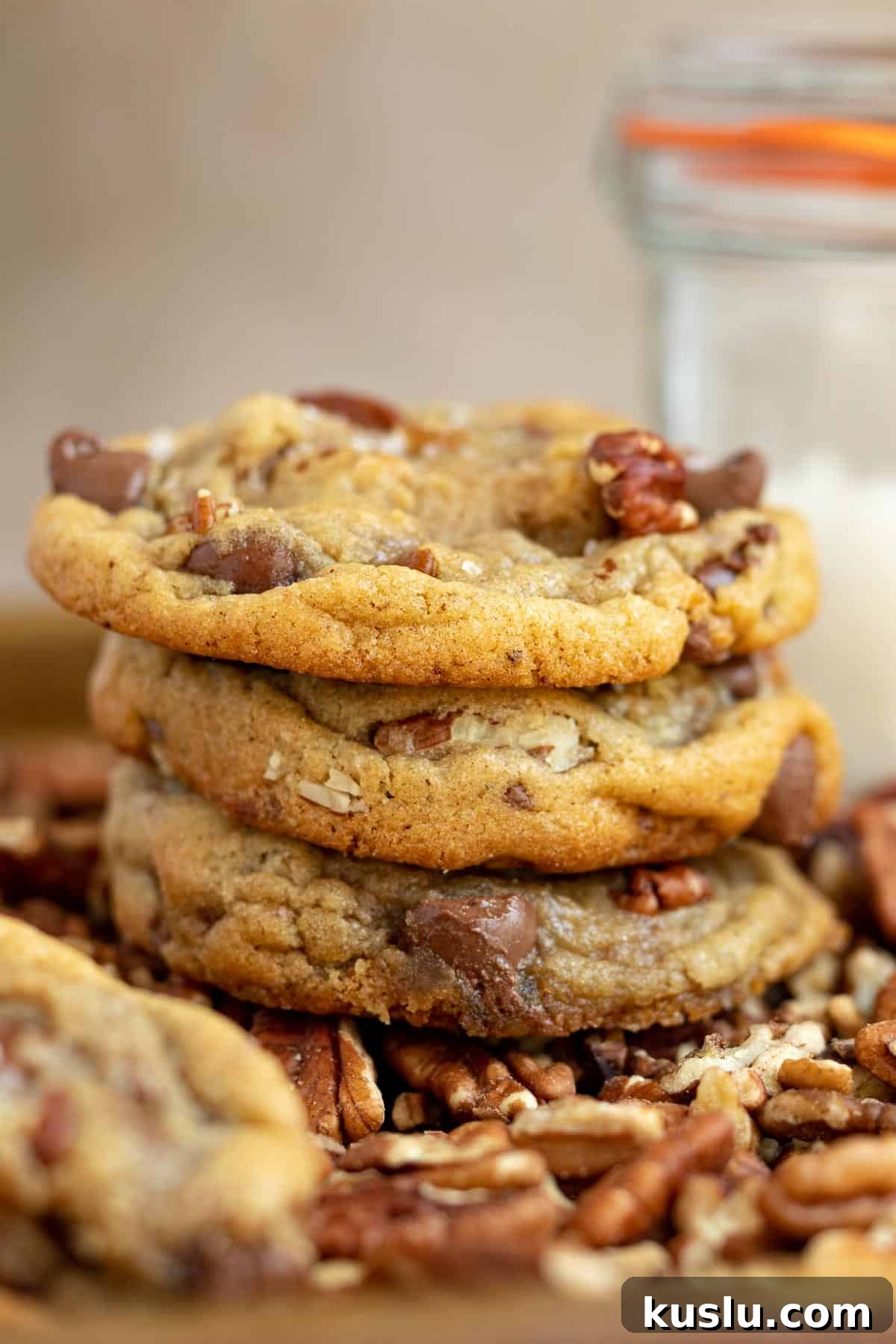 a stack of pecan chocolate chip cookies with a glass container of sea salt in the background