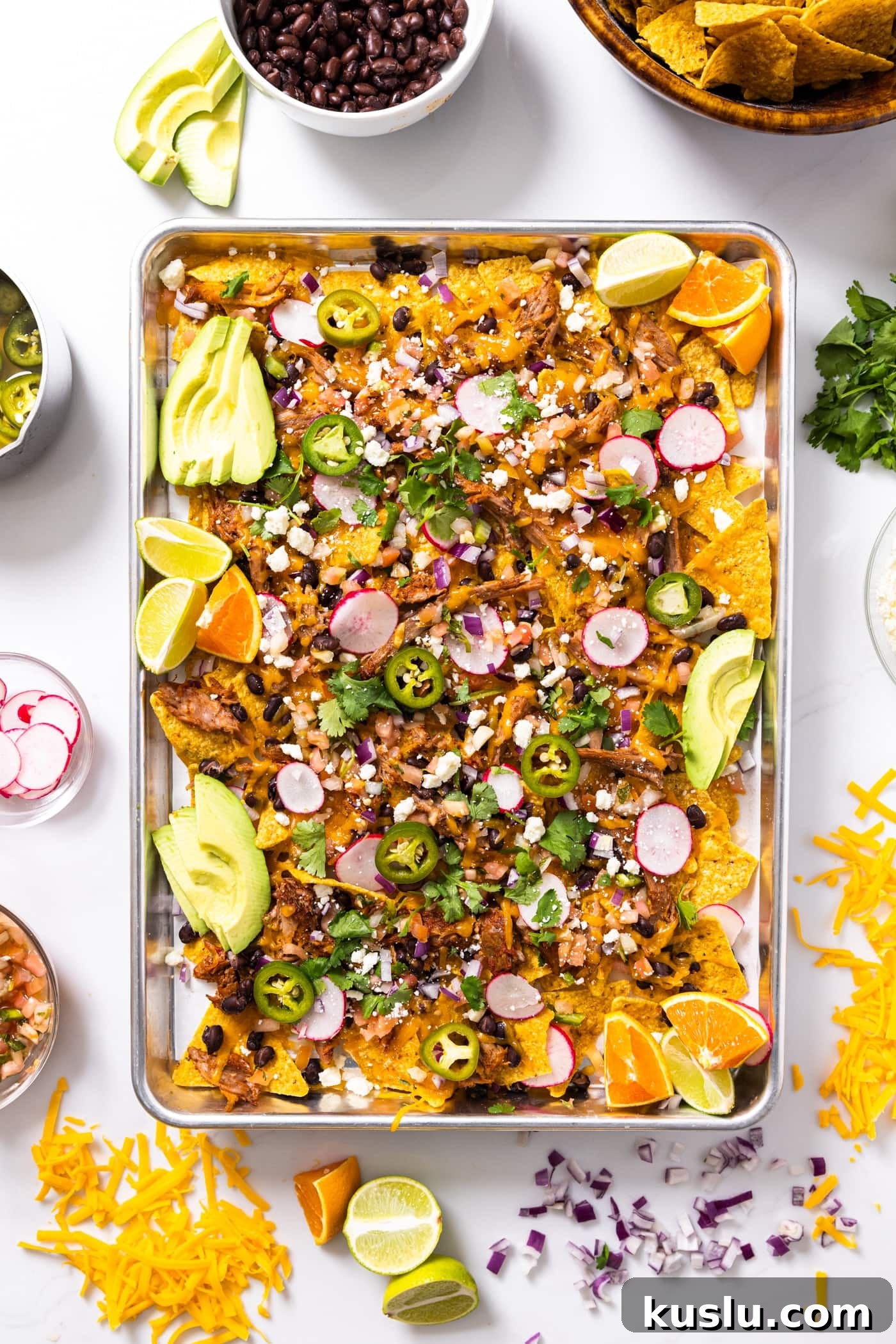 Pulled Pork Sheet-Pan Nachos: Loaded Crowd-Pleasing Recipe 3 Top down view of metal sheet pan sitting on white countertop filled with tortilla chips and pulled pork with lots of toppings on top along with shredded cheese