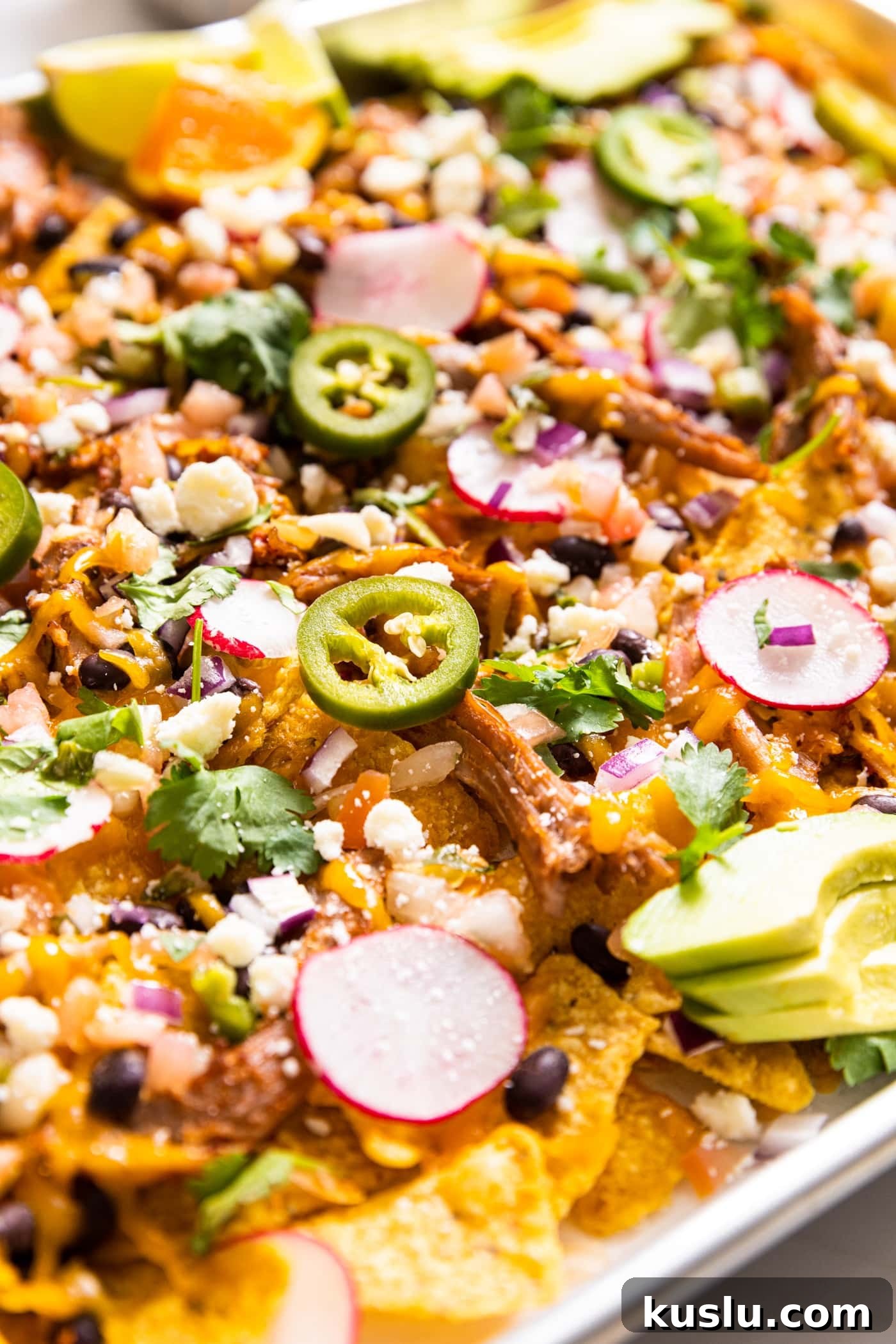 Pulled Pork Sheet-Pan Nachos: Loaded Crowd-Pleasing Recipe 4 Large metal sheet pan with lots of tortilla chips underneath topped with pulled pork and lots of toppings and shredded cheese