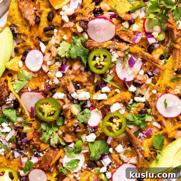 Pulled Pork Sheet-Pan Nachos: Loaded Crowd-Pleasing Recipe 6 Top down view of metal sheet pan filled with tortilla chips and pulled pork with melted shredded cheese on top along with other toppings as well as avocado