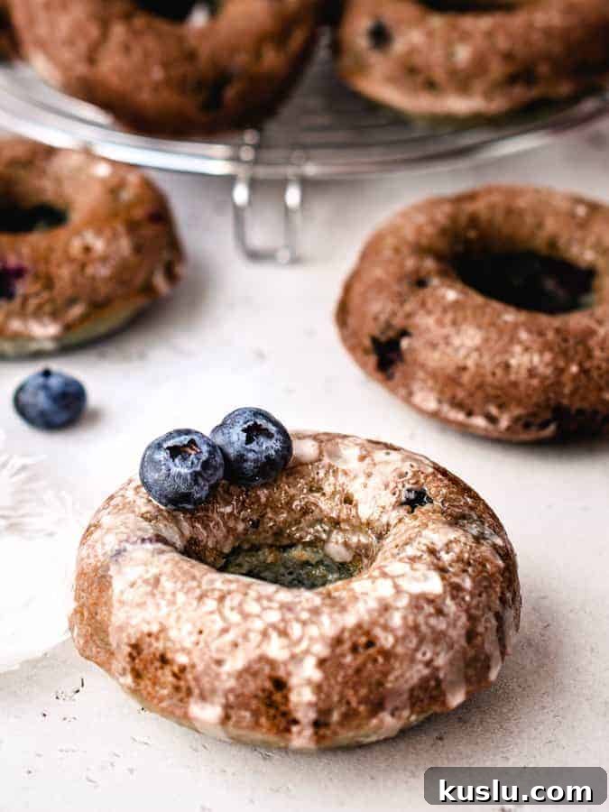 Close up for blueberry cake donut with glaze on it and 2 blueberries sitting on top