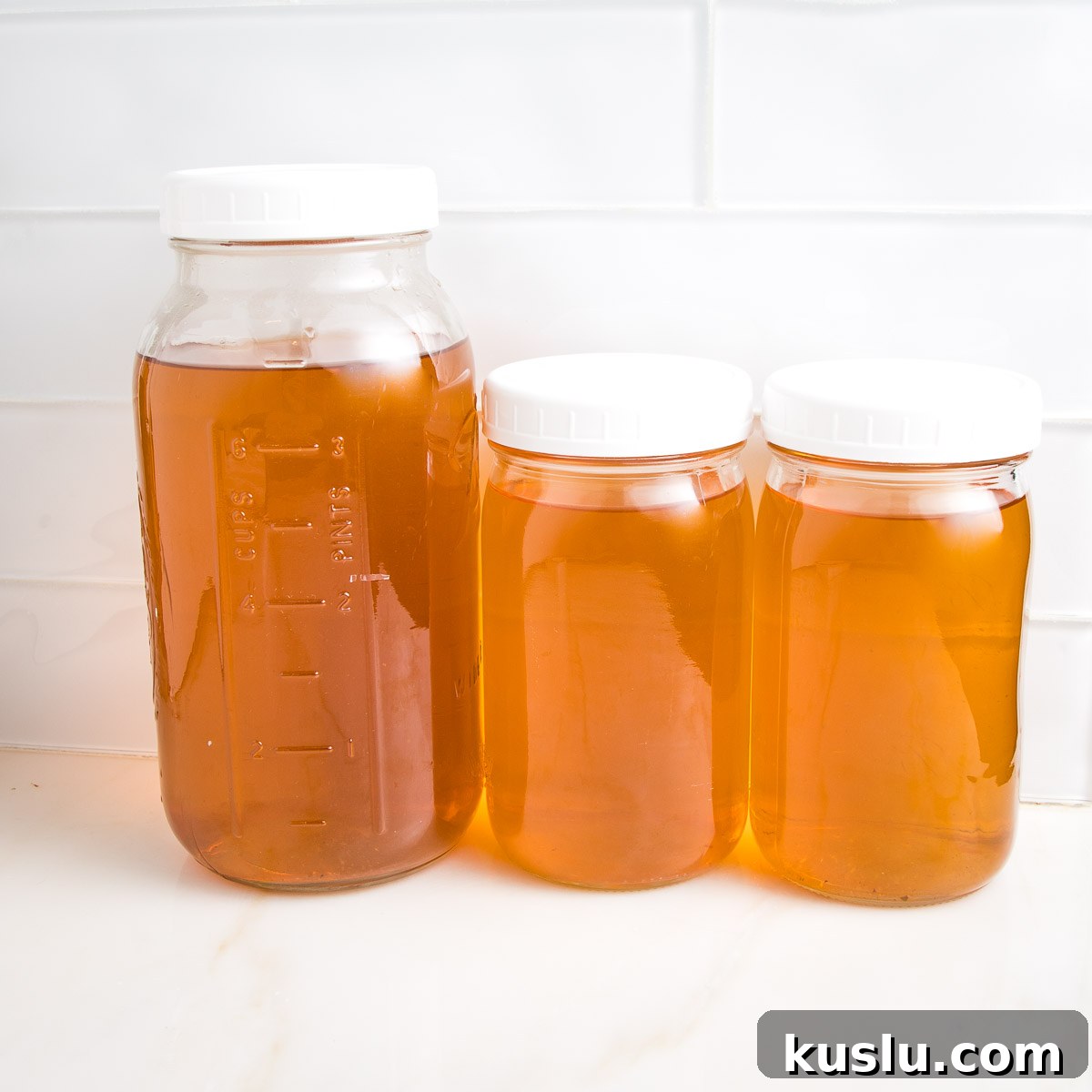 How to Make Flavorful Homemade Vegetable Broth from Scratch 8 Three glass mason jars with white plastic tops. All are filled with golden colored liquid...homemade vegetable broth.