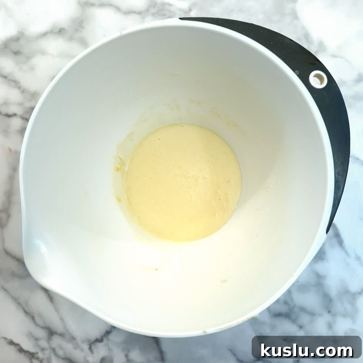 Eggs and sugar whisked together in a white mixing bowl.