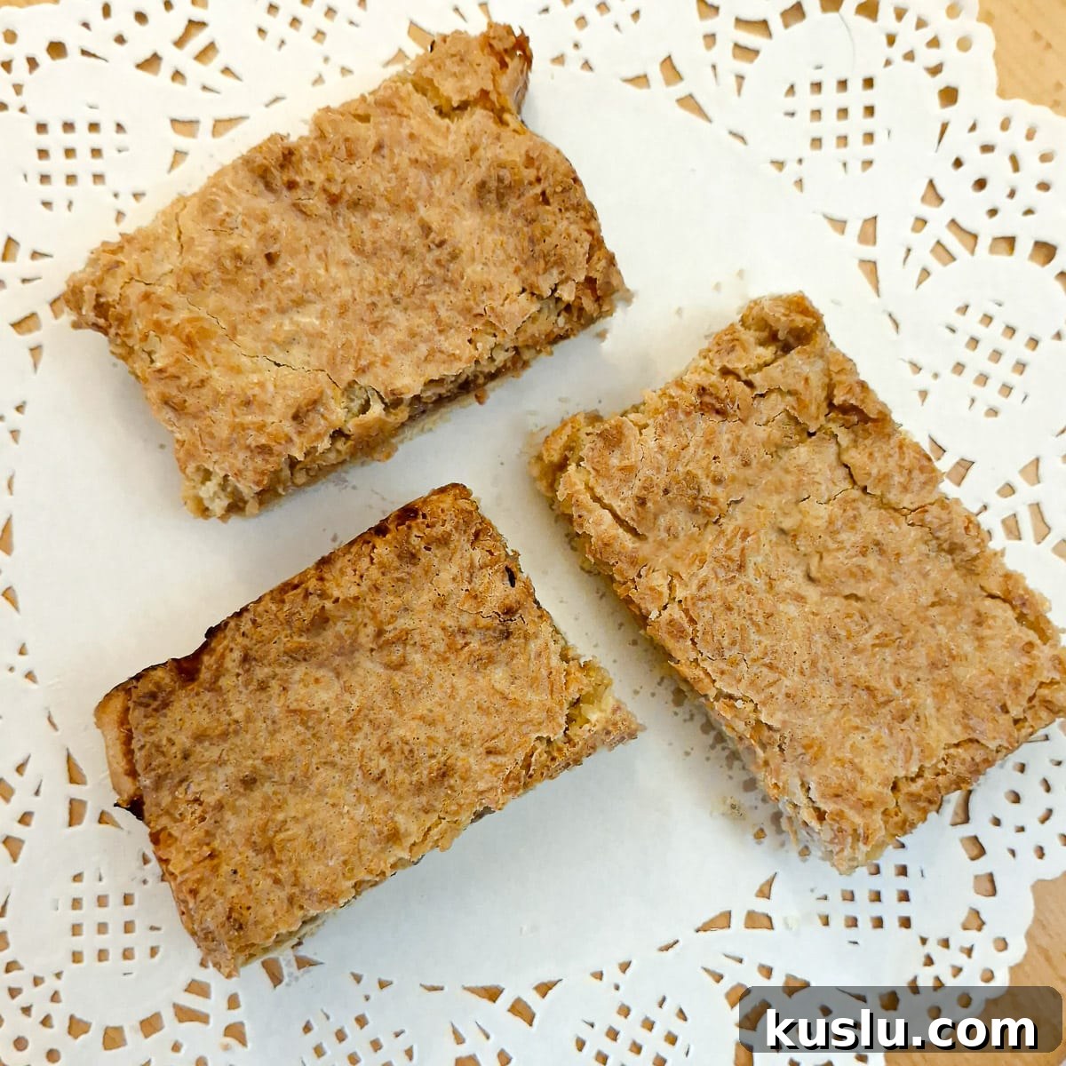 Three slices of coconut  jam slice on a white paper doily.