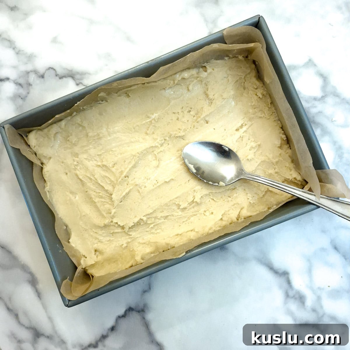 The sticky dough being spread into the baking dish with the help of a tablespoon.