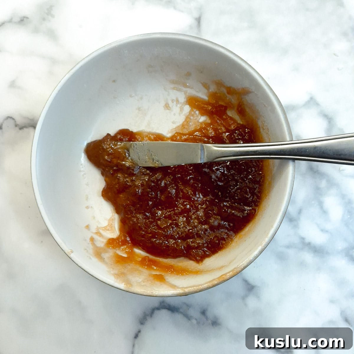 Strawberry jam being softened in a white bowl.