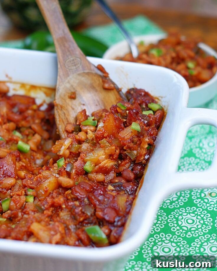 A close up of a spoonful of baked beans with pineapple, bacon, bell pepper and onion.