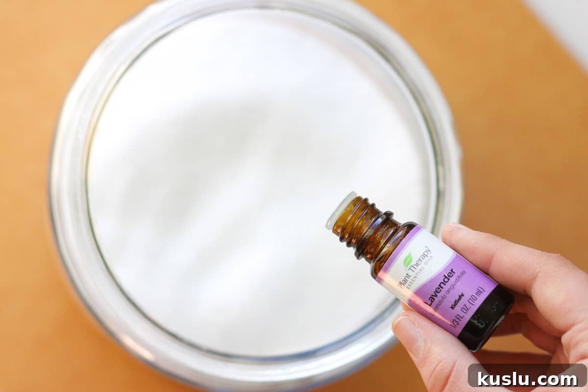 lavender essential oil being added to a glass jar of baking soda mixed with Epsom salts