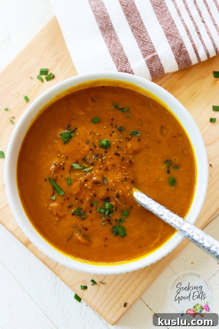 Beautiful orange pumpkin soup served in a white bowl and garnished with fresh chives