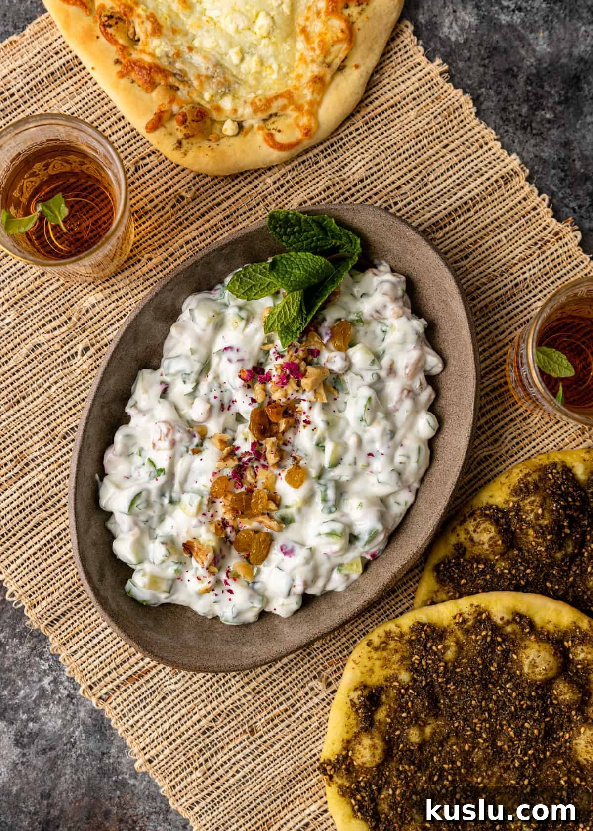 overhead: Middle Eastern table with zaatar bread, persian cucumber yogurt dip, and glass of tea on woven placemat