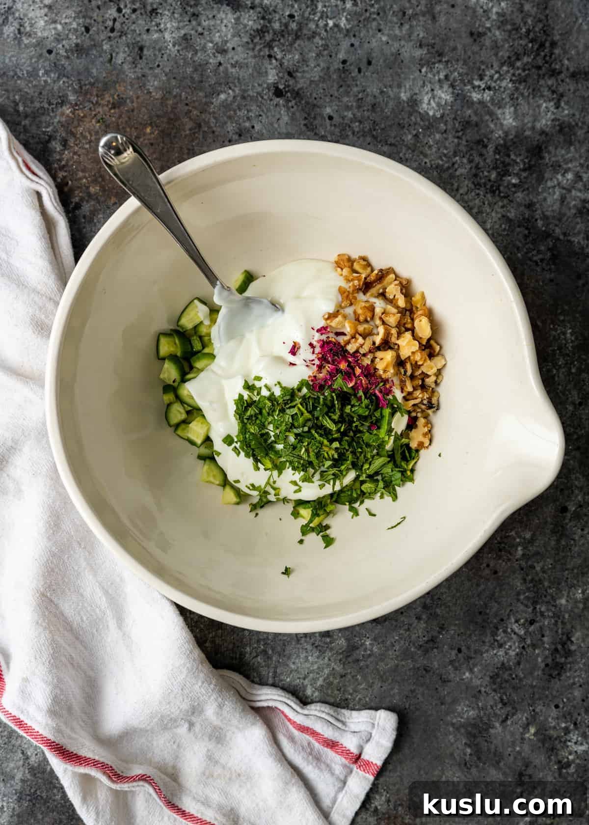 overhead: diced Persian cucumbers, walnuts, rose petals and yoghurt in white bowl for salad