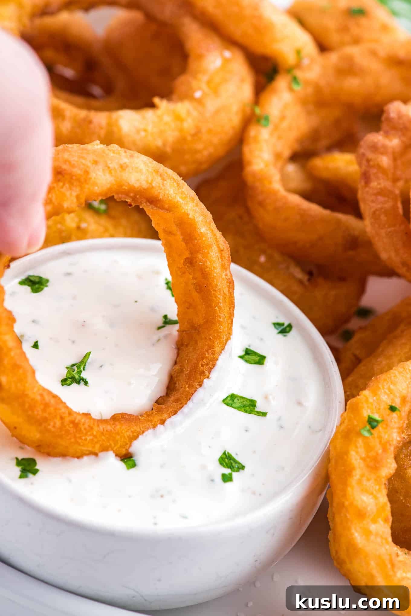 Crispy Frozen Onion Rings in the Air Fryer: Quick Recipe Guide 7 A hand dipping an onion ring into a creamy dip.