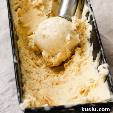 Creamy Homemade Peach Ice Cream Recipe for Summer 12 Ice cream scoop with a scoop of ice cream sitting inside a container full of peach ice cream.
